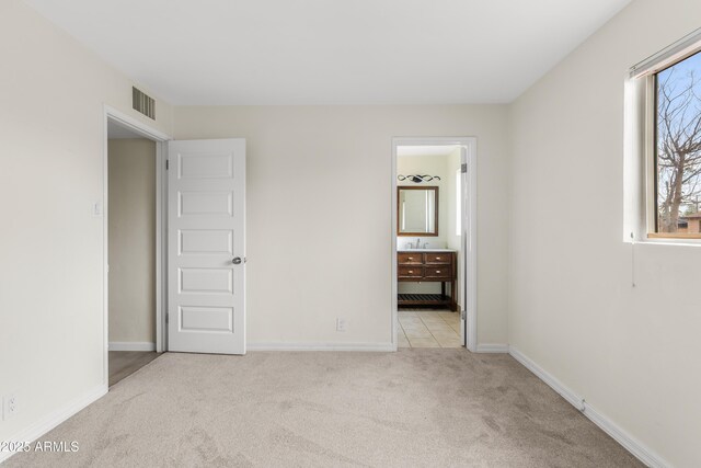 unfurnished bedroom featuring baseboards, visible vents, ensuite bathroom, carpet floors, and a sink