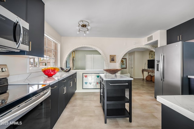 kitchen with light stone counters, visible vents, stainless steel appliances, and dark cabinets