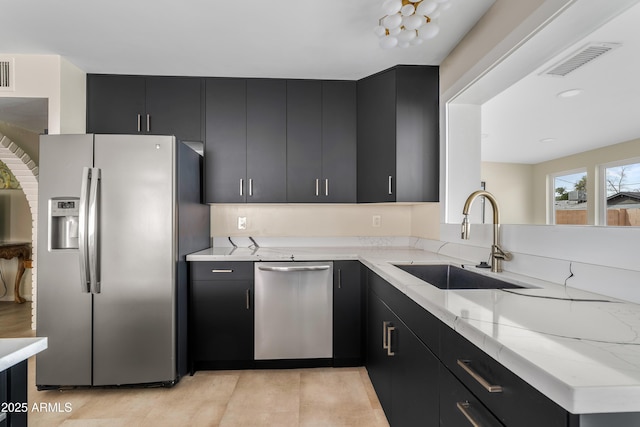 kitchen with stainless steel appliances, dark cabinetry, a sink, and visible vents