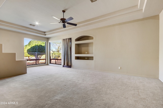 unfurnished living room with carpet, ceiling fan, built in shelves, and a tray ceiling