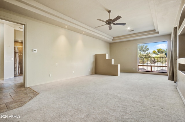 unfurnished room with a raised ceiling, light carpet, and ceiling fan