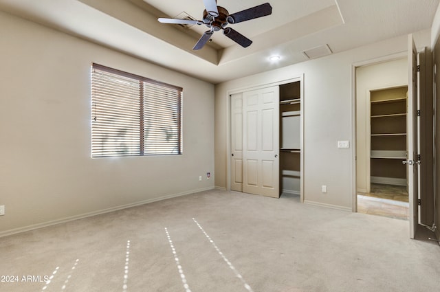 unfurnished bedroom featuring a closet, a tray ceiling, ceiling fan, and light colored carpet