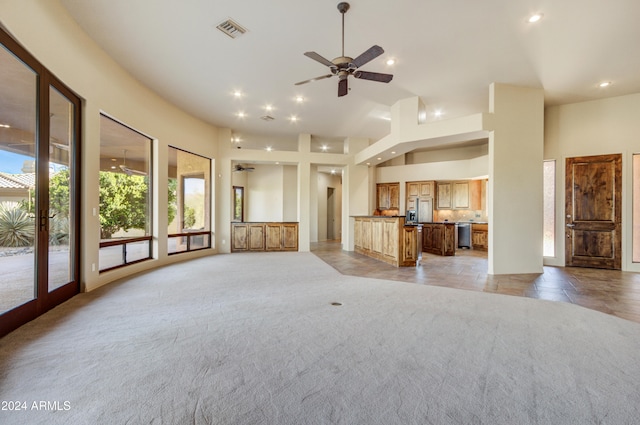 unfurnished living room featuring ceiling fan, light colored carpet, a high ceiling, and french doors