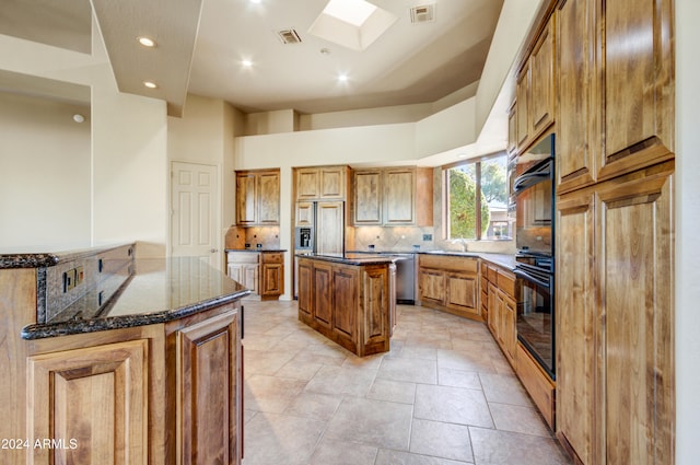 kitchen with tasteful backsplash, black double oven, light tile patterned floors, dark stone countertops, and a center island