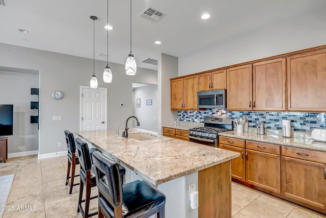 16426 W Piccadilly Rd, Goodyear, AZ 85395 - kitchen with stainless steel appliances, tasteful backsplash, light stone counters, a kitchen island with sink, and brown cabinets