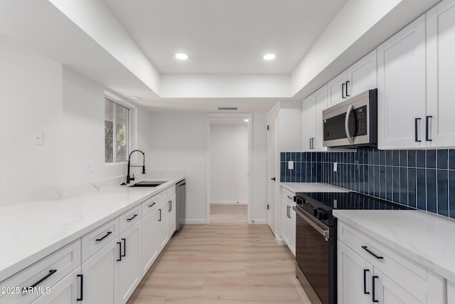 kitchen with light stone countertops, white cabinetry, sink, and stainless steel appliances