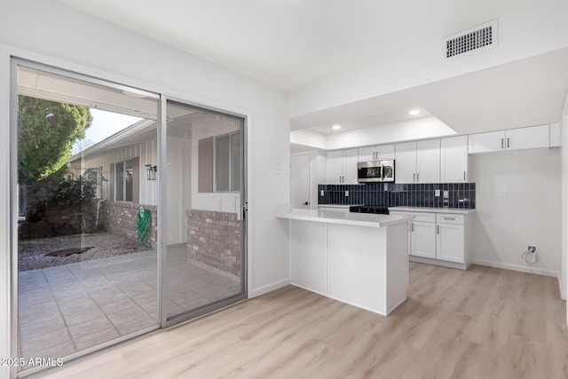 kitchen featuring kitchen peninsula, backsplash, white cabinetry, and light hardwood / wood-style floors