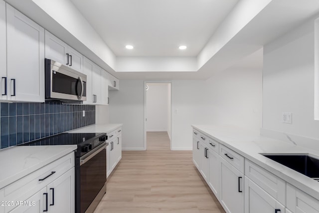 kitchen with white cabinetry, backsplash, light wood-type flooring, light stone counters, and black / electric stove