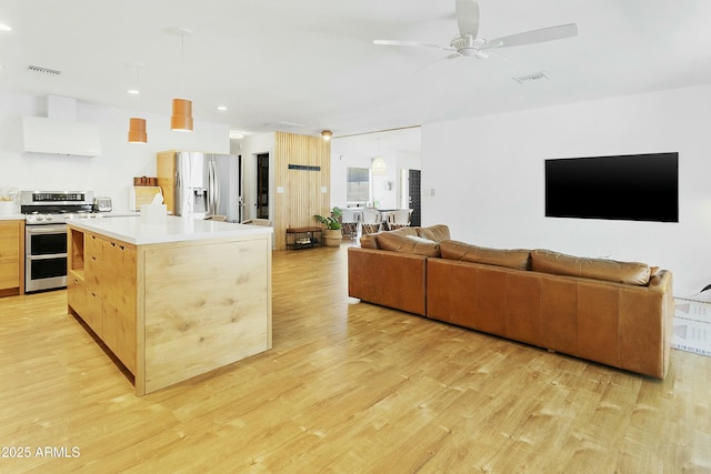 kitchen with wall chimney range hood, open floor plan, visible vents, and stainless steel appliances