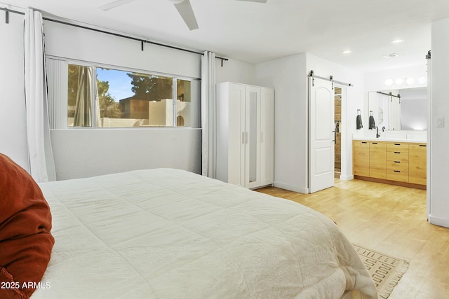 bedroom featuring recessed lighting, light wood-type flooring, a barn door, and ensuite bathroom