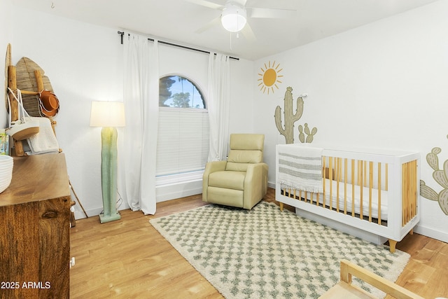 bedroom with baseboards, a nursery area, and wood finished floors