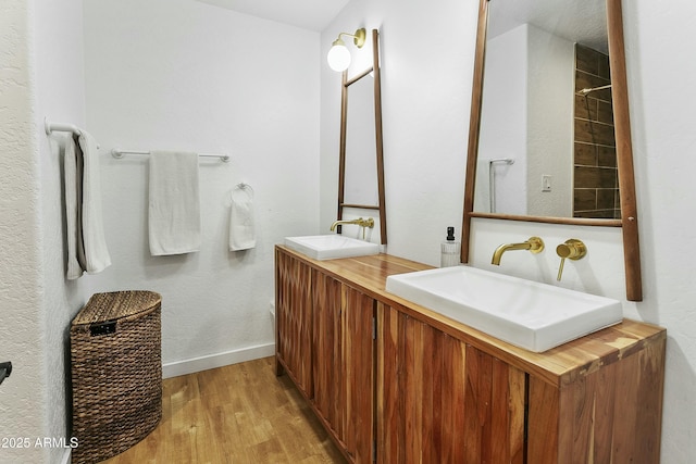 full bathroom featuring baseboards, double vanity, a sink, and wood finished floors