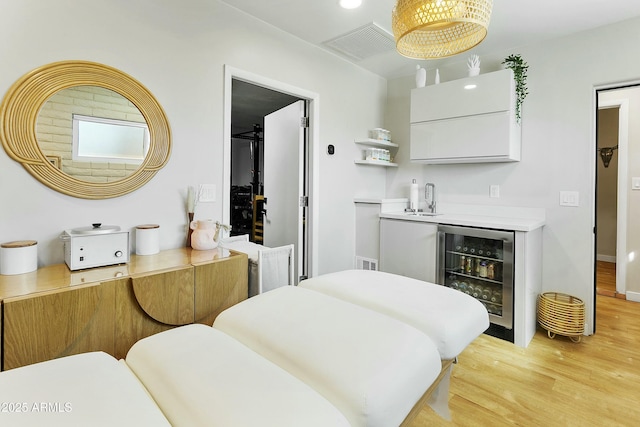 bedroom featuring visible vents, wine cooler, a sink, light wood-type flooring, and indoor wet bar