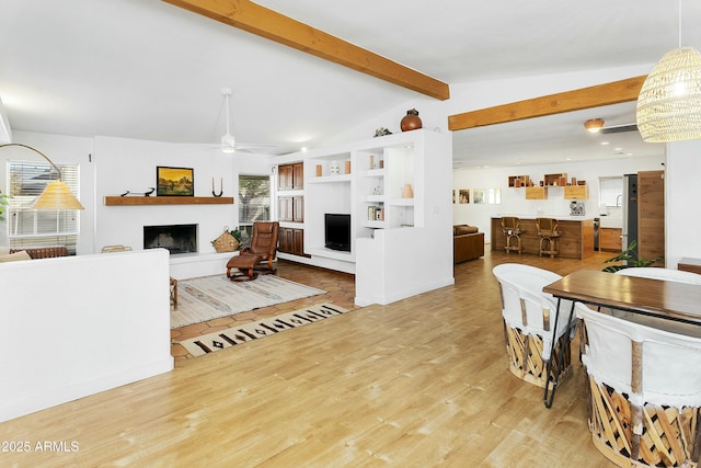 living area with vaulted ceiling with beams, wood finished floors, a fireplace with raised hearth, and ceiling fan