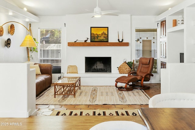 living room with a fireplace with raised hearth and a ceiling fan