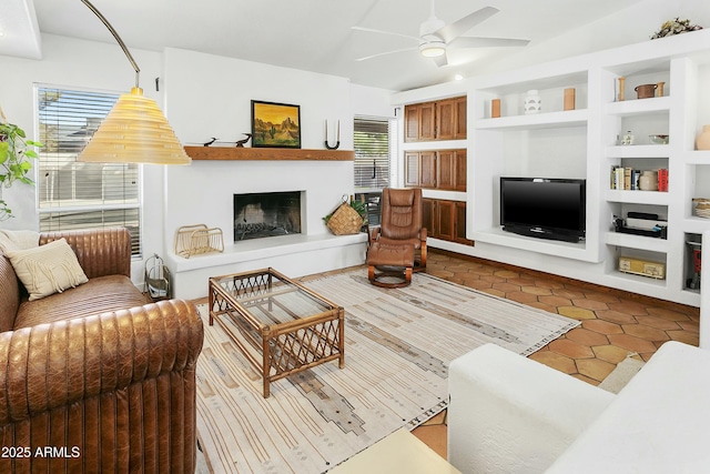 living area featuring dark tile patterned flooring, a fireplace with raised hearth, built in shelves, and ceiling fan