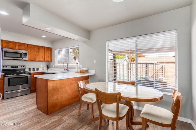 kitchen with kitchen peninsula, sink, light wood-type flooring, and appliances with stainless steel finishes