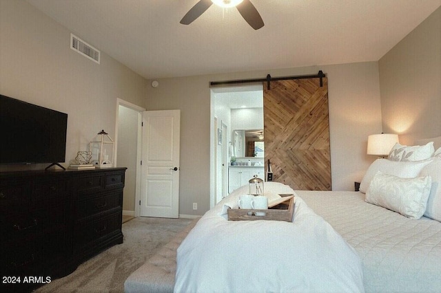 carpeted bedroom with a barn door, ceiling fan, and connected bathroom