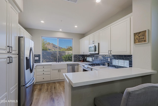 kitchen with white cabinetry, kitchen peninsula, appliances with stainless steel finishes, and light wood-type flooring