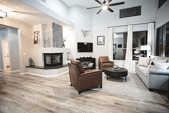 living room with a high ceiling, a tiled fireplace, wood-type flooring, and ceiling fan