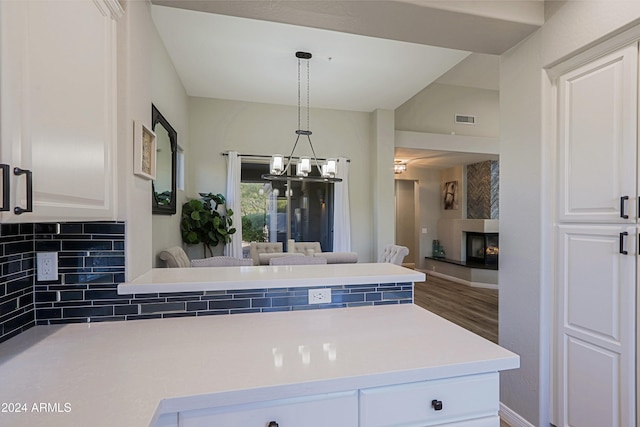 kitchen with kitchen peninsula, hanging light fixtures, hardwood / wood-style floors, white cabinets, and decorative backsplash