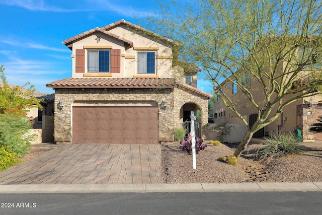 mediterranean / spanish-style home with an attached garage, a tiled roof, stone siding, decorative driveway, and stucco siding