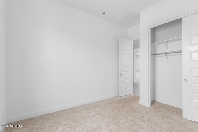 unfurnished bedroom with light colored carpet and a closet