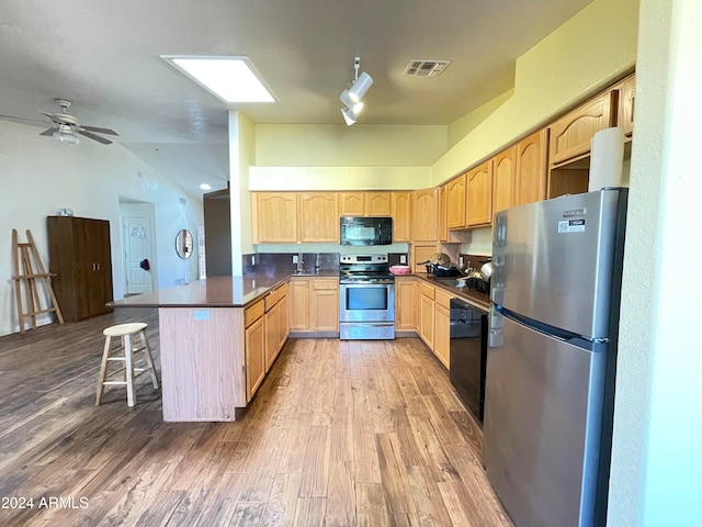 kitchen featuring black appliances, kitchen peninsula, a kitchen breakfast bar, light brown cabinetry, and wood-type flooring