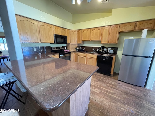 kitchen featuring lofted ceiling, kitchen peninsula, black appliances, a kitchen breakfast bar, and light hardwood / wood-style flooring