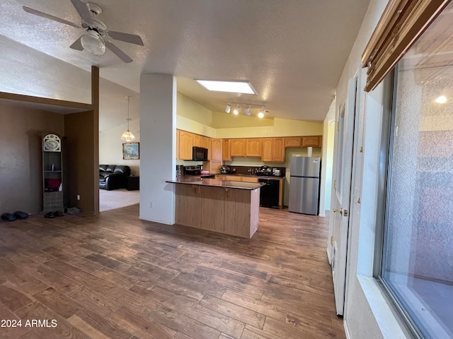 kitchen with stainless steel appliances, kitchen peninsula, vaulted ceiling with skylight, ceiling fan, and dark wood-type flooring