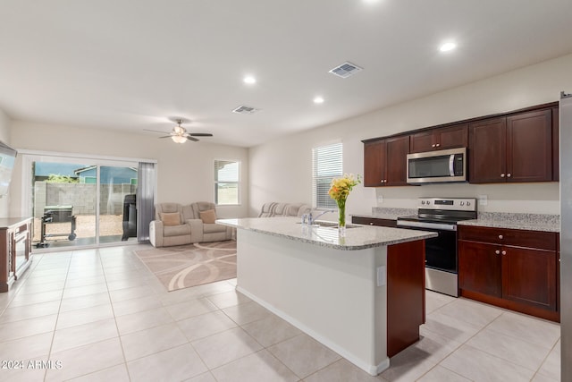 kitchen featuring light stone countertops, appliances with stainless steel finishes, ceiling fan, light tile flooring, and a kitchen island with sink