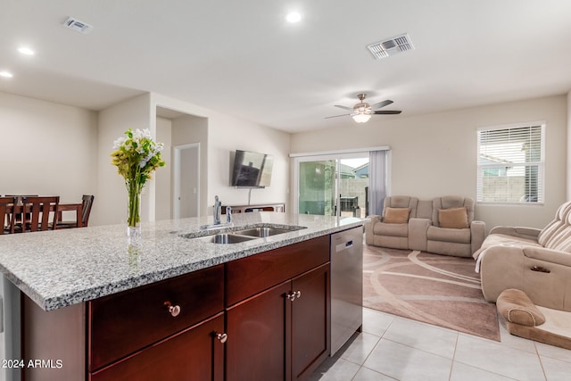 kitchen with ceiling fan, an island with sink, light stone counters, light tile floors, and stainless steel dishwasher