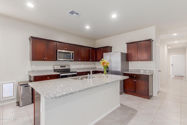 kitchen featuring light stone counters, stainless steel appliances, sink, and an island with sink