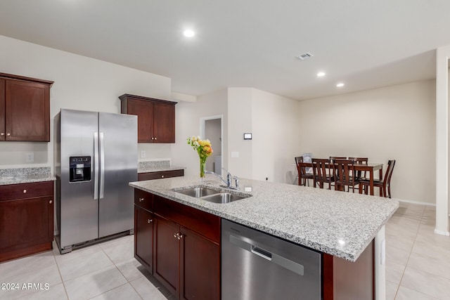 kitchen featuring appliances with stainless steel finishes, light stone counters, light tile flooring, and a kitchen island with sink