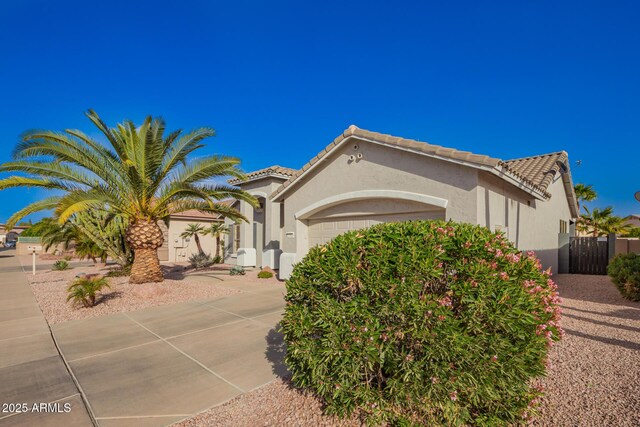 view of front facade featuring a garage, a tiled roof, fence, and stucco siding