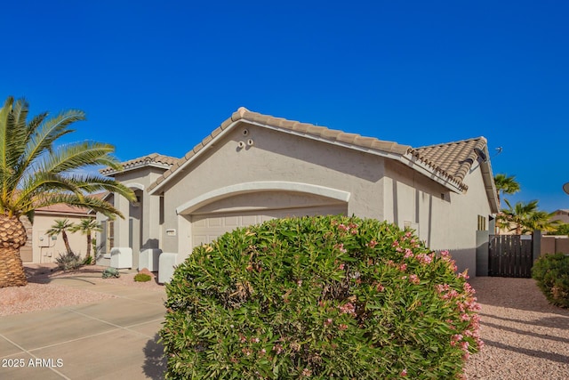 view of front of property featuring a tiled roof, an attached garage, fence, and stucco siding