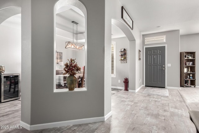 foyer entrance featuring beverage cooler, arched walkways, wood finished floors, and baseboards