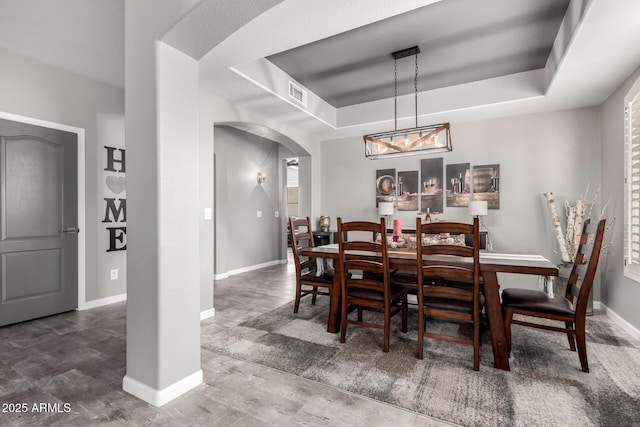 dining area with arched walkways, a raised ceiling, visible vents, and baseboards