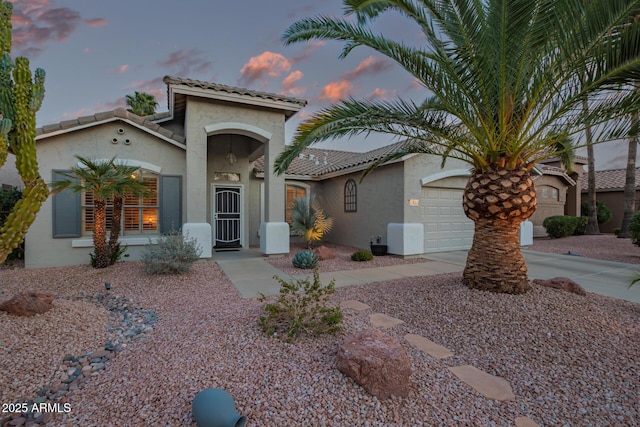 mediterranean / spanish-style home with a garage, driveway, a tile roof, and stucco siding