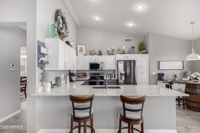 kitchen featuring visible vents, lofted ceiling, a peninsula, stainless steel appliances, and a sink