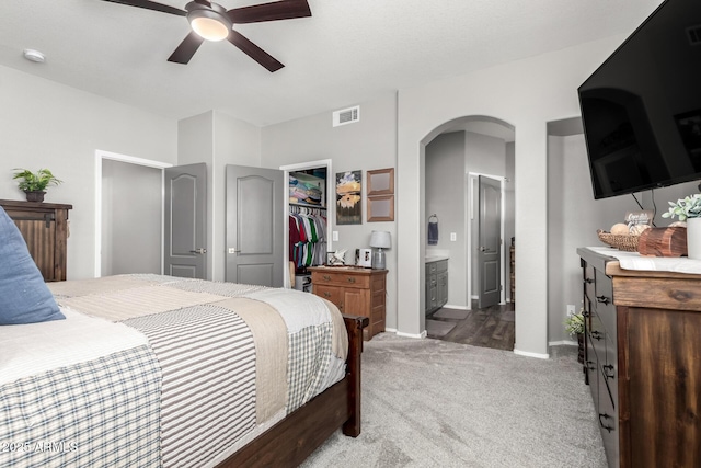 bedroom featuring visible vents, arched walkways, ensuite bathroom, a walk in closet, and carpet floors