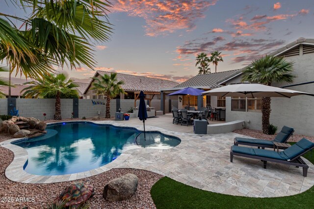 pool at dusk featuring a fenced backyard, a fenced in pool, and a patio