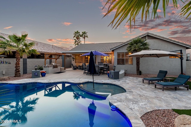 pool at dusk with exterior kitchen, a patio area, a fenced backyard, and a fenced in pool