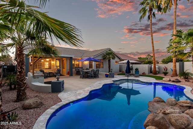 pool at dusk with a fenced in pool, outdoor dining space, a fenced backyard, and a patio