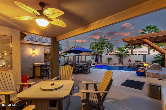 patio terrace at dusk with a fenced in pool, a fenced backyard, outdoor dry bar, exterior kitchen, and outdoor dining space