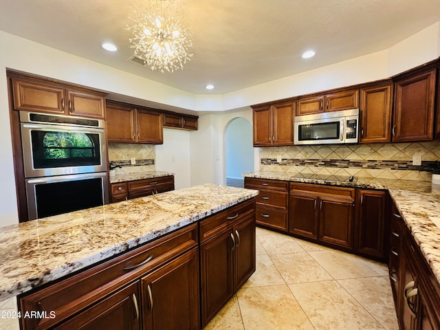 kitchen featuring pendant lighting, a notable chandelier, light stone counters, and appliances with stainless steel finishes