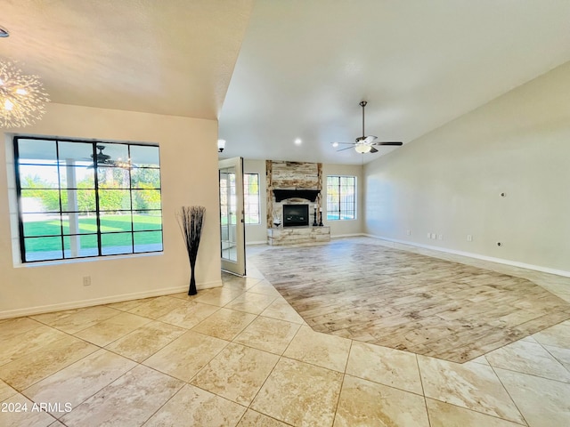 unfurnished living room featuring ceiling fan with notable chandelier, a healthy amount of sunlight, a fireplace, and vaulted ceiling