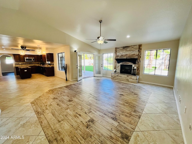 unfurnished living room with a stone fireplace, ceiling fan, a healthy amount of sunlight, and lofted ceiling