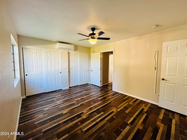 unfurnished bedroom featuring ceiling fan, dark wood-type flooring, a wall unit AC, a textured ceiling, and two closets