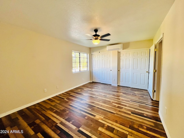 unfurnished bedroom featuring dark wood-type flooring, ceiling fan, a textured ceiling, a wall mounted AC, and multiple closets